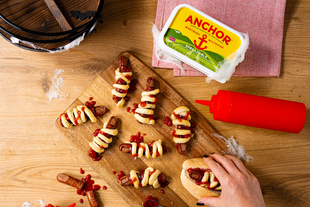 Wooden chopping board covered in spooky hotdogs wrapped in pastry