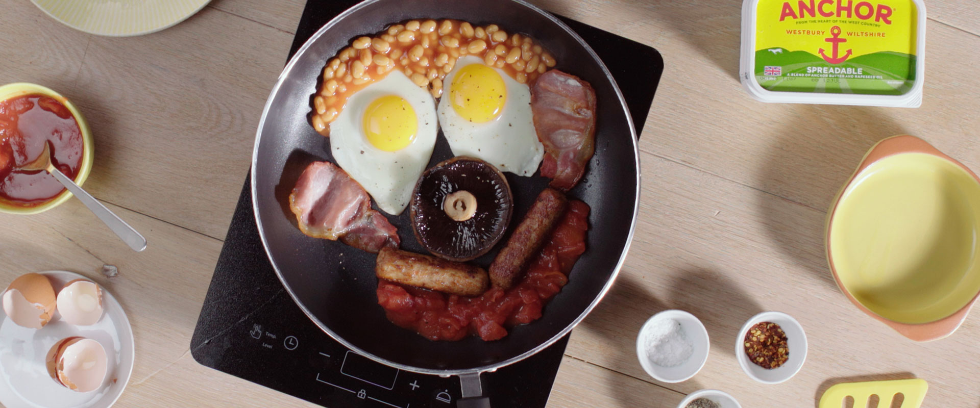 Tomatoes, 2 sausages, 2 eggs, baked beans, a mushroom and 2 rashers of bacon in a pan